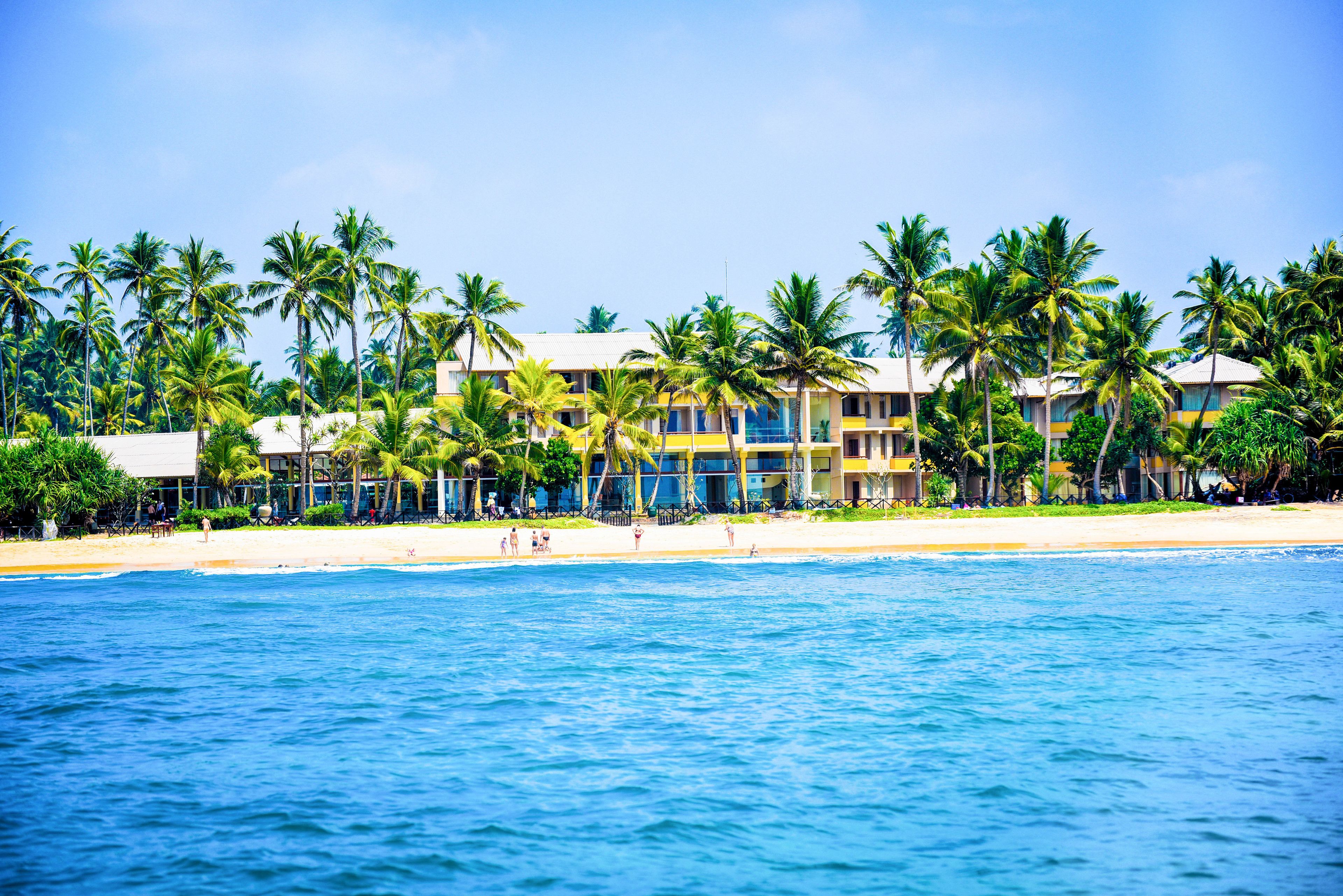 A beachfront hotel with multiple stories, palm trees, and a sandy beach.