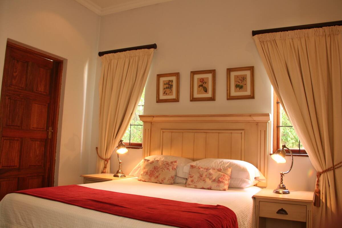A bedroom with a wooden headboard, a bed with floral bedding, two bedside tables with lamps, and three framed pictures on the wall.
