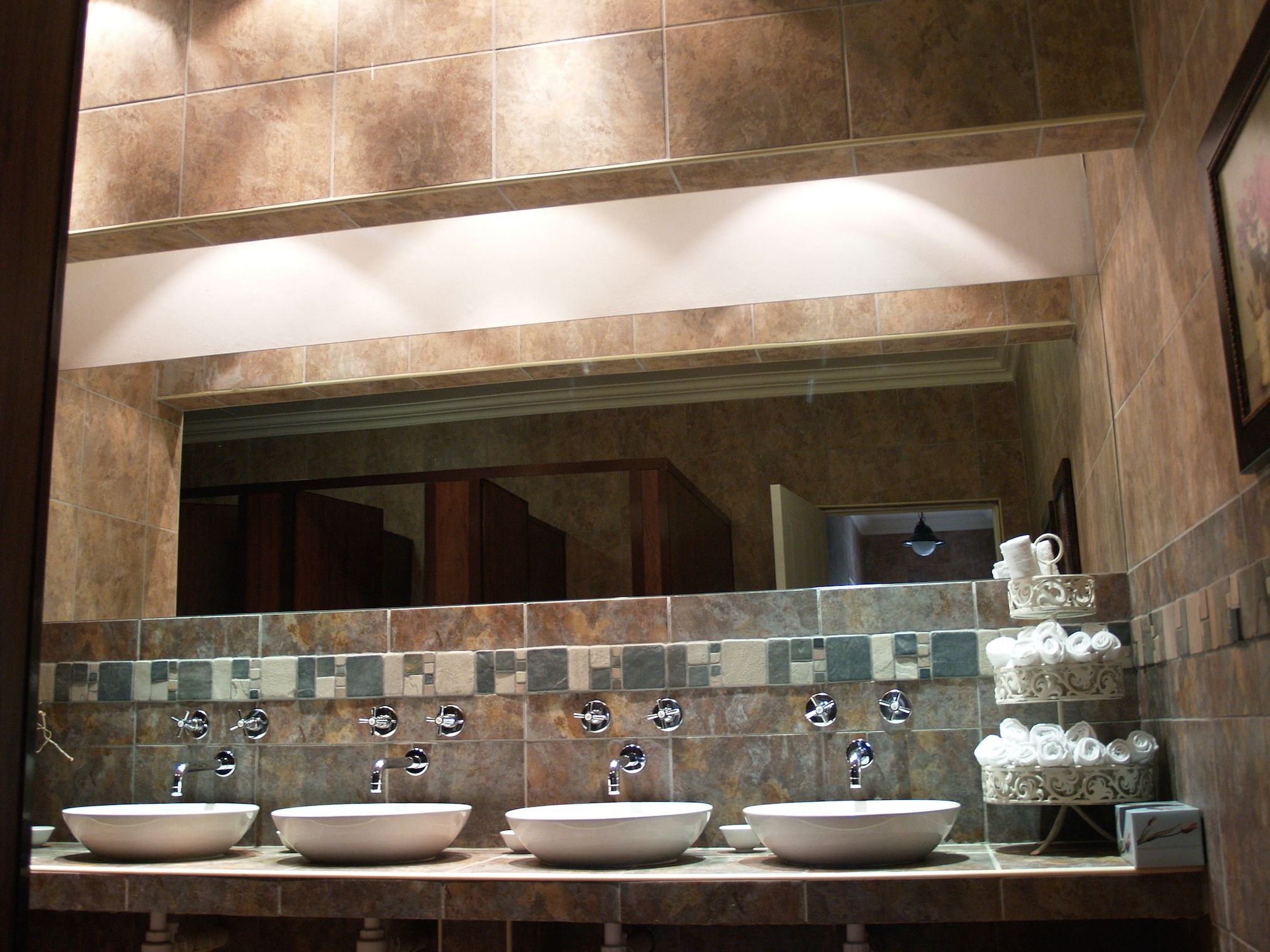 A bathroom with three sinks, a large mirror, and a tiled backsplash.