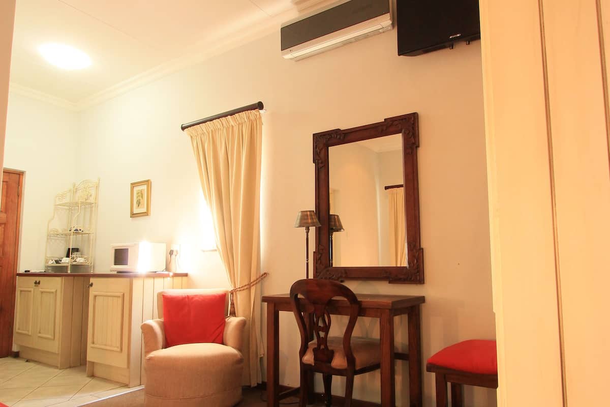A bedroom with a bed, a desk, a chair, a mirror, a television, and a window with curtains.