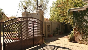 Una entrada cerrada con un portón de hierro decorativo, un farol y un camino de ladrillo que lleva a un edificio con tejado de azulejos.