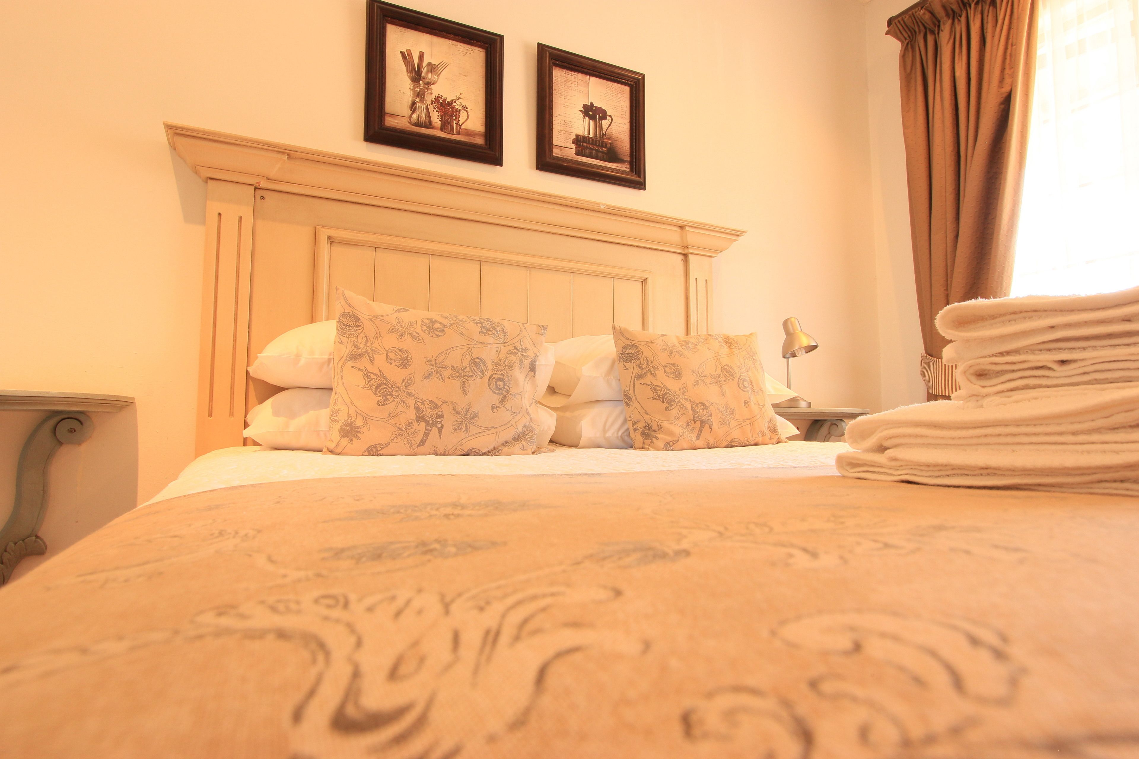 Una cama bien hecha con almohadones estampados, un cabecero y una pila de toallas dobladas.
