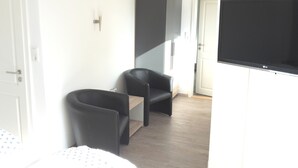 A modern hotel room with a bed, two black chairs, a small wooden table, a flat-screen TV, and a wardrobe. - Pension Marktblick (Friedrichstadt)