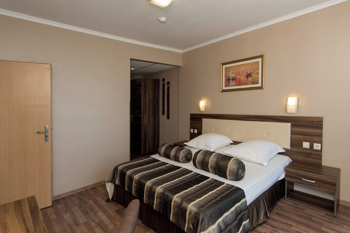 Ein Hotelzimmer mit Bett, Nachttischen, einer Tür und einem Bild an der Wand.