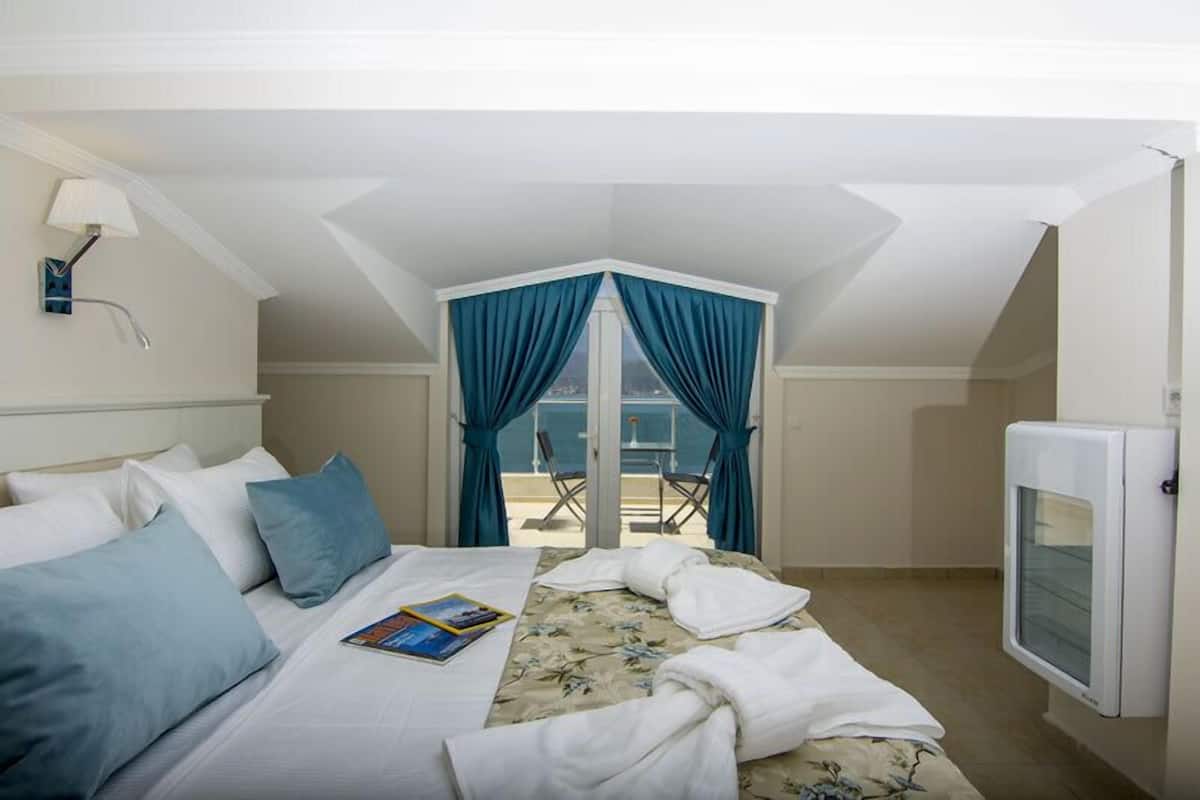 A hotel room with a bed, a TV, and a balcony with blue curtains.