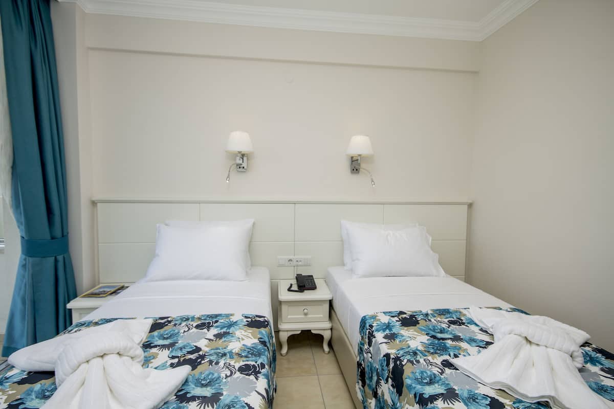 A hotel room with two beds, a nightstand with a phone, and a window with curtains.