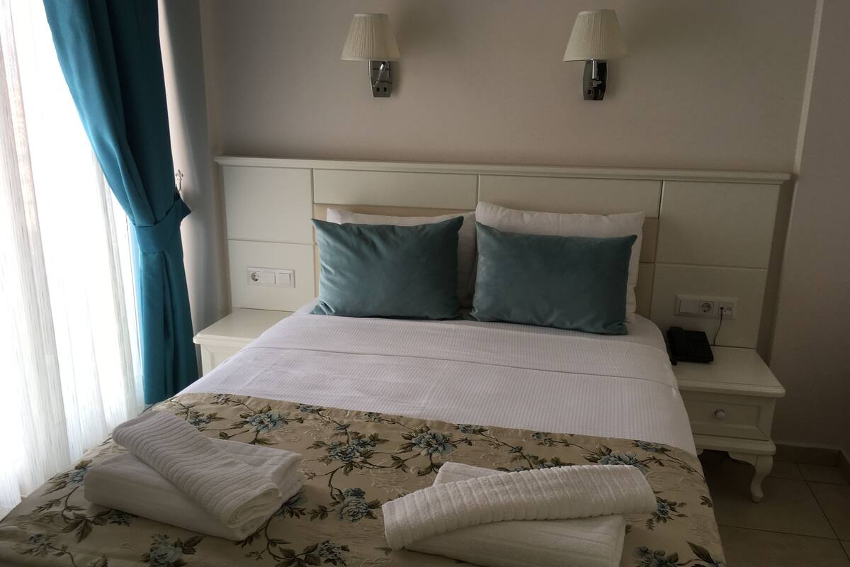 A neatly made bed with floral bedding, two bedside lamps, and a bedside phone on a white nightstand.