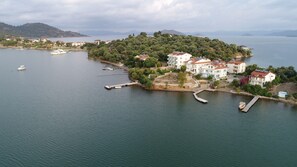 An aerial view of a coastal area with a small island featuring residential buildings, docks, and boats. - Sovalye Hotel (Fethiye)