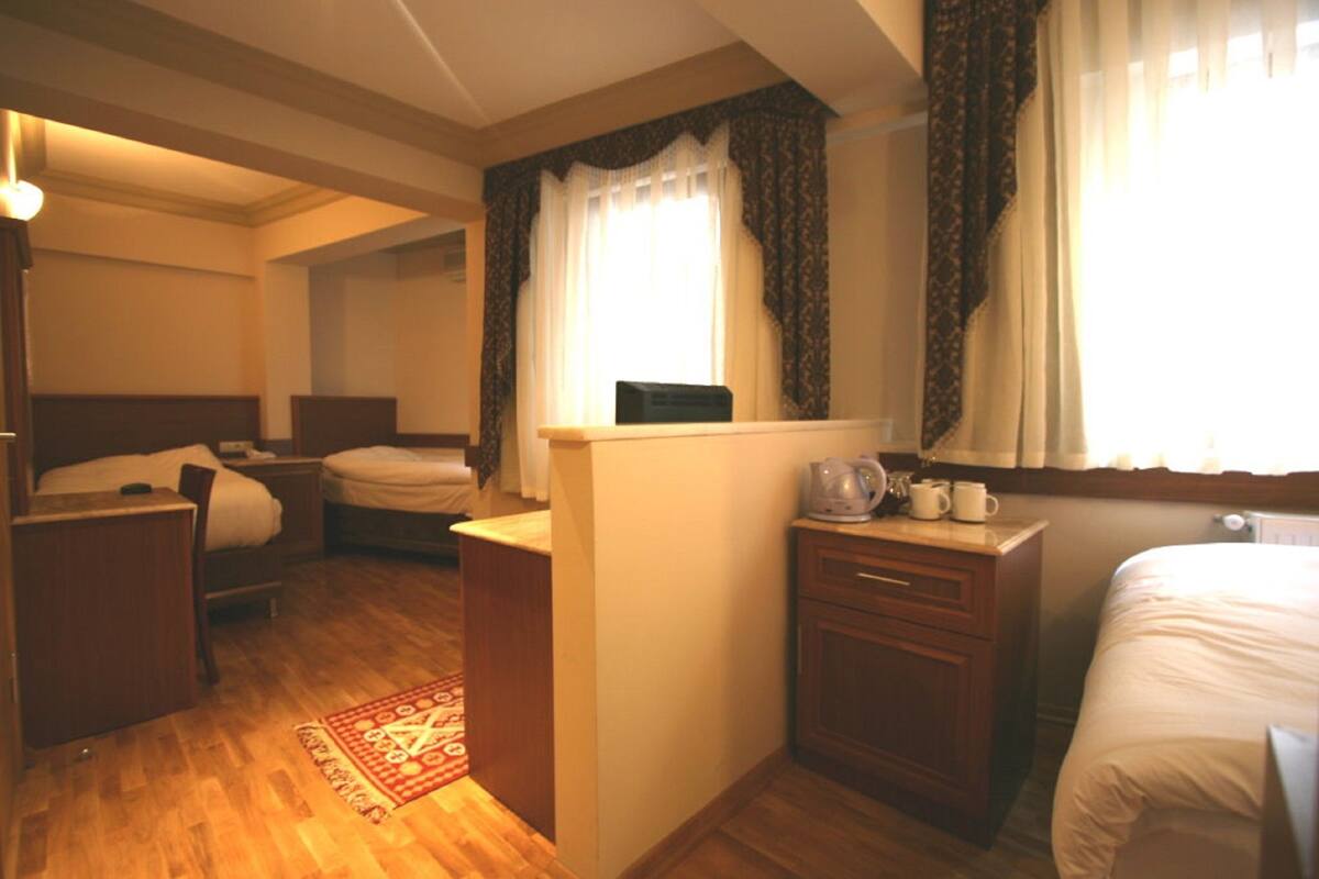 Une chambre d’hôtel avec deux lits, une petite kitchenette, une fenêtre avec des rideaux et un plancher en bois.