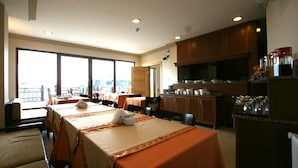 A hotel dining area with tables set for a meal, a kitchen area with cabinets and appliances, and large windows offering a view. - Grand Peninsula Hotel (Istanbul)