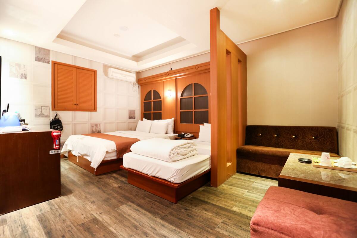 A hotel room with two beds, a wooden desk, a brown sofa, and a small table.