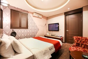 A hotel room with a bed, a TV, a chair, and a wardrobe.