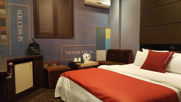 A hotel room with a bed, a nightstand, a desk, and a wall with motivational posters.
