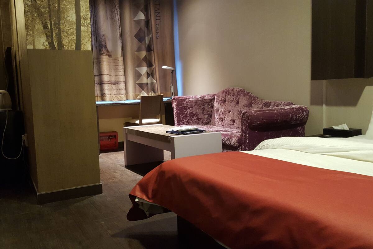 A hotel room with a bed, a desk, a chair, and a sofa.