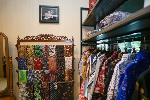 A clothing store with a variety of patterned fabrics displayed on a wooden stand and racks of clothes.