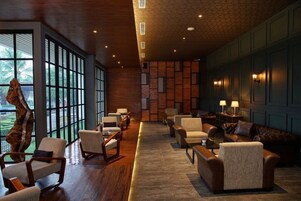 A spacious lobby with a wooden floor, a large tree sculpture, and a seating area with sofas and chairs.