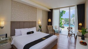 Habitación de hotel con una cama grande, un escritorio con teléfono, una silla, una mesa con fruta y vistas a una piscina y zonas verdes.