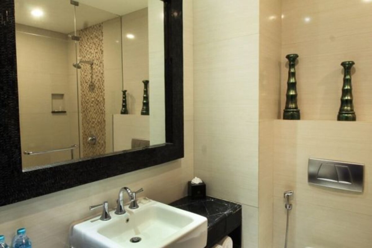 Une salle de bain équipée d’un lavabo, d’un miroir, d’une douche et de deux vases décoratifs accrochés au mur.