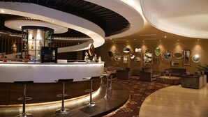 Un área de bar moderna con una barra curva, taburetes y una variedad de espejos decorativos y obras de arte en la pared.