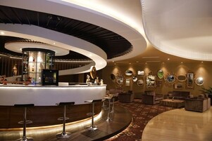 A modern bar area with a curved counter, bar stools, and a variety of decorative mirrors and wall art.