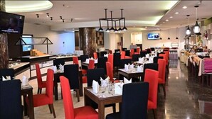 A restaurant with red and black chairs, tables set with white tablecloths, and a modern chandelier.