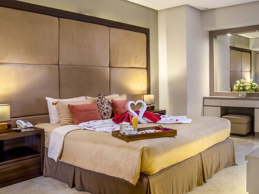 Habitación de hotel con una cama grande, una mesita de noche con lámpara, teléfono y una bandeja con productos para el desayuno.