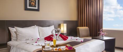 A hotel room with a neatly made bed, a tray of breakfast, a framed picture on the wall, and a window with curtains.