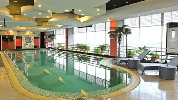An indoor swimming pool with a glass barrier, lounge chairs, and large windows.