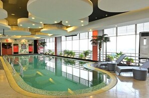 Una piscina interior con barrera de cristal, sillas de descanso y ventanas amplias.