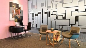 A modern reception area with a pink wall, a large abstract painting, and a geometric wall design.