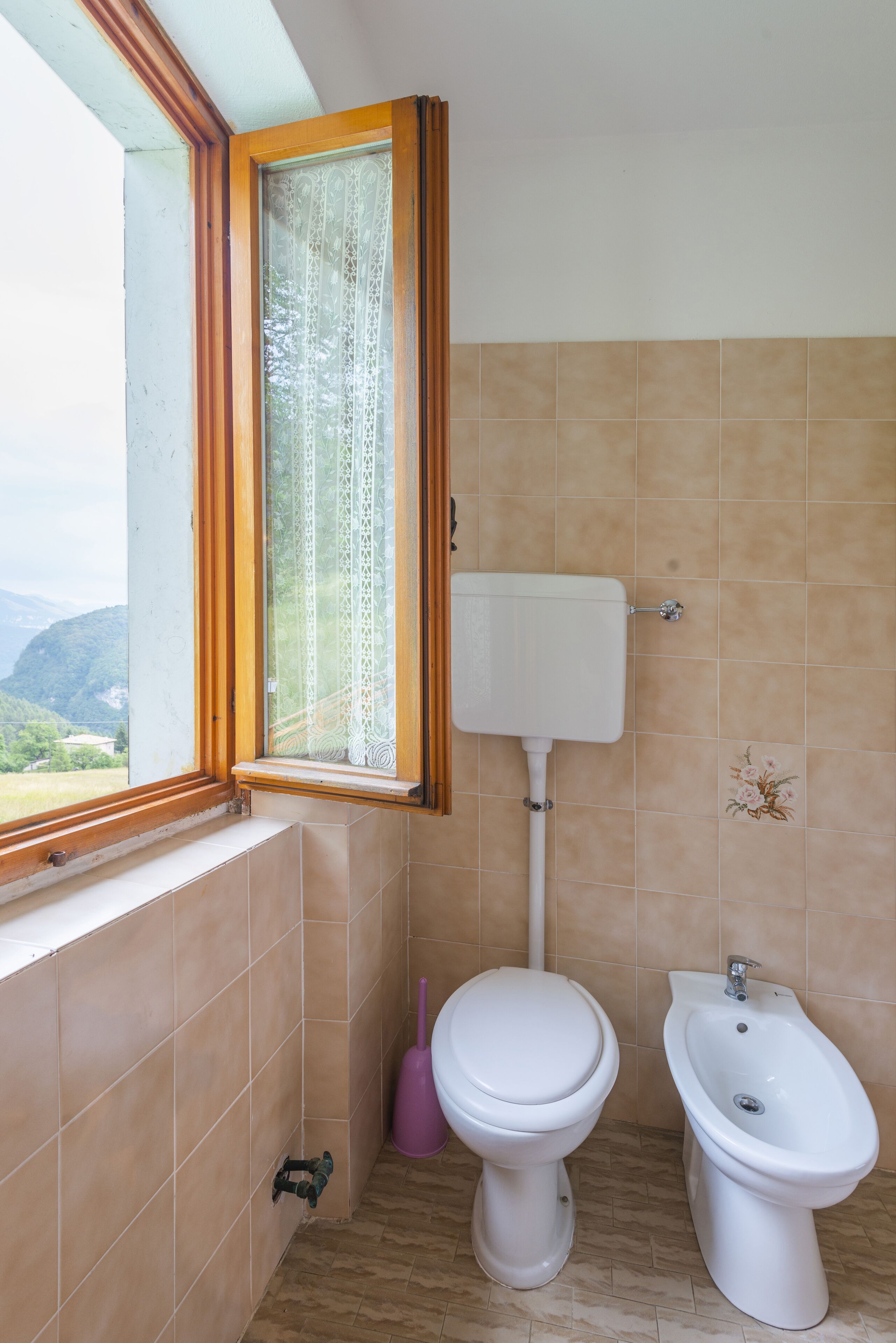 A bathroom with a window, a toilet, and a bidet.