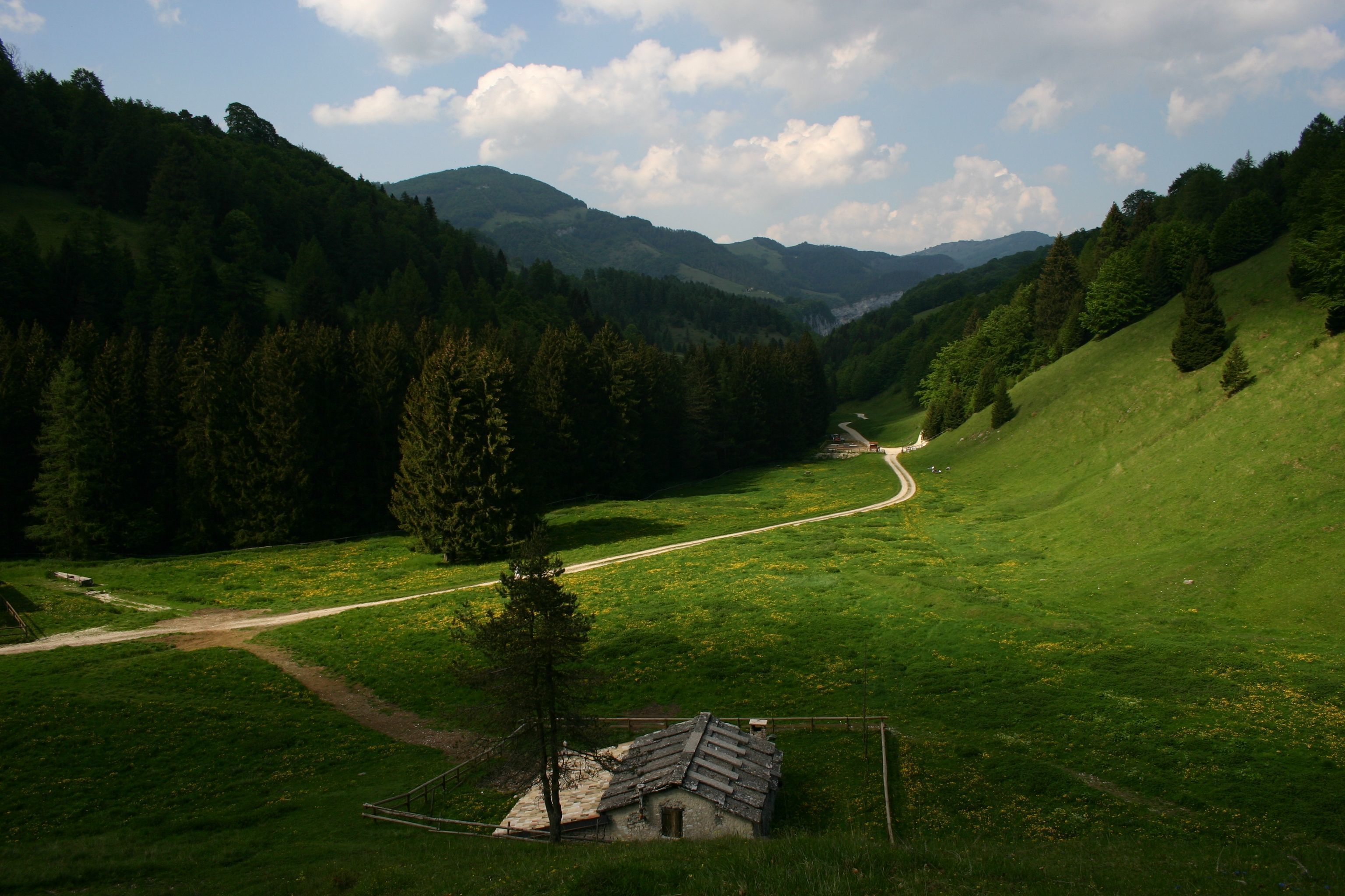 Paisaje rural con una casa pequeña, un sendero de tierra y una carretera que atraviesa un valle.