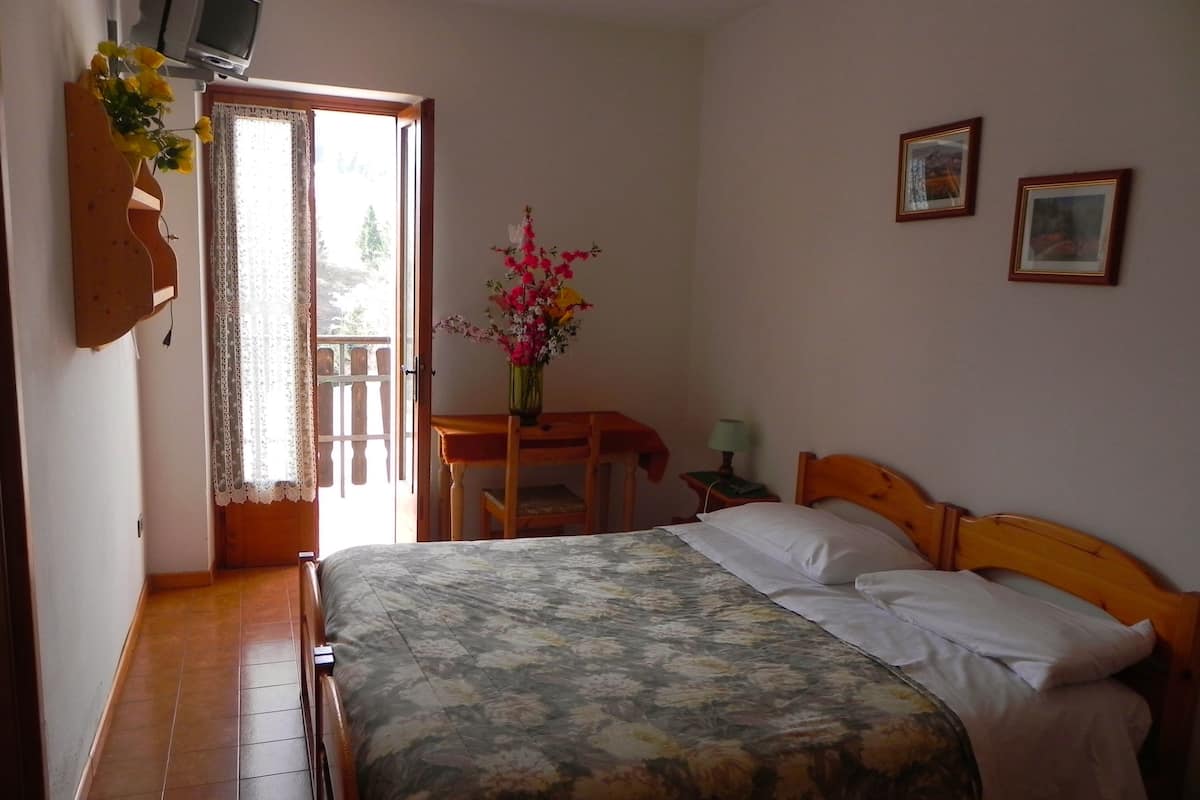 A bedroom with a bed, a wooden desk, a chair, a nightstand, and a TV.