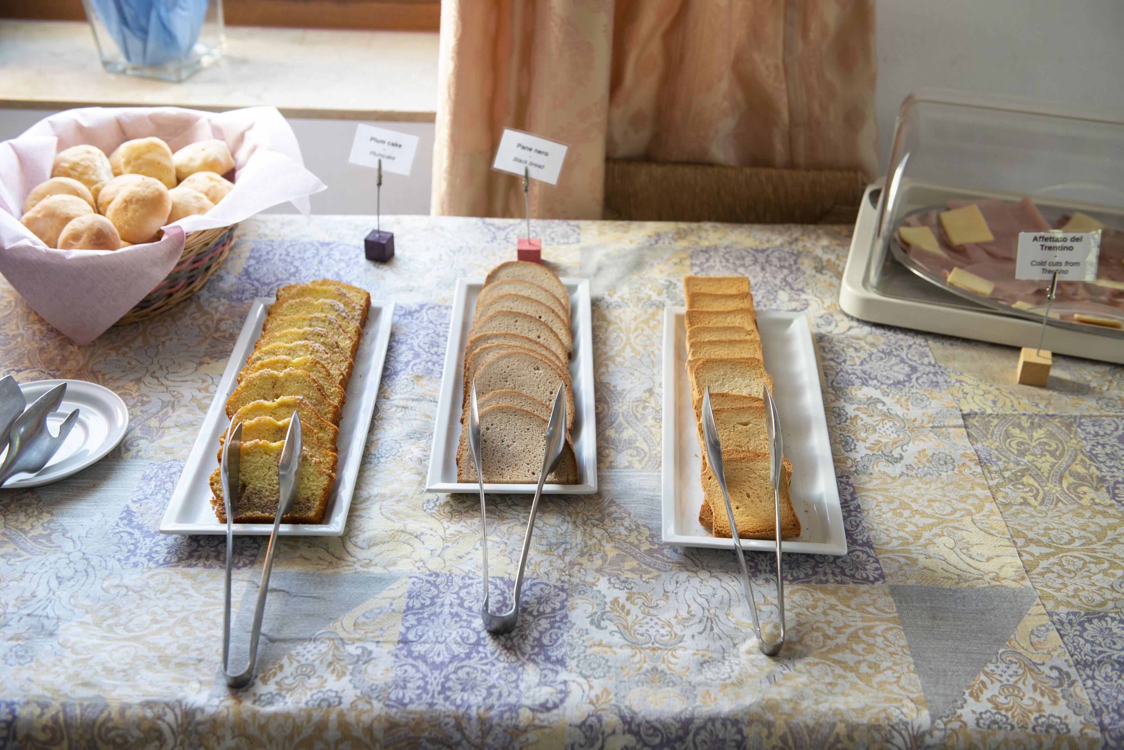 A buffet table with various food items, including bread and pastries, arranged on plates with serving utensils.