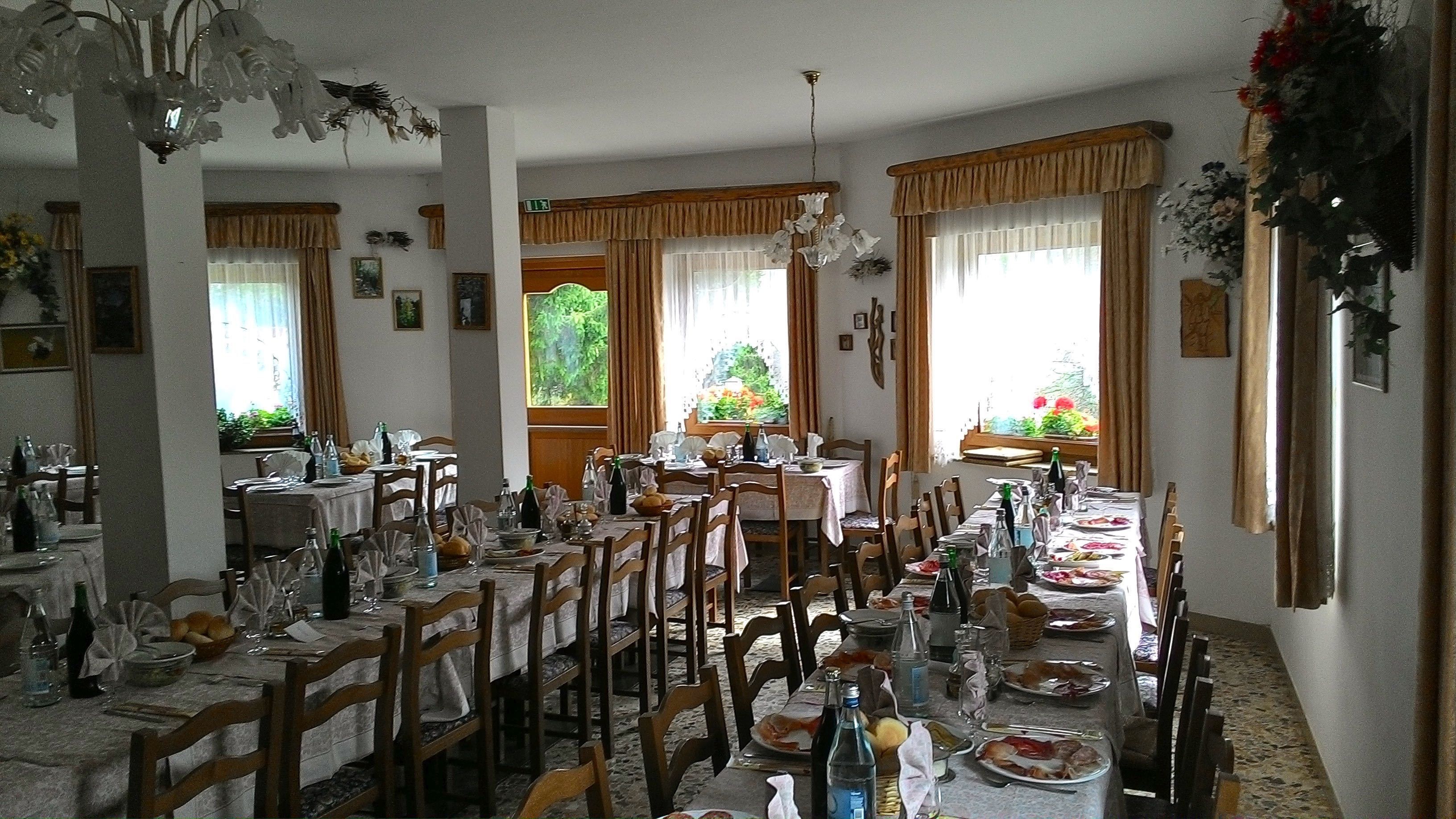 Un comedor con varias mesas dispuestas para comer, sillas de madera y una araña.