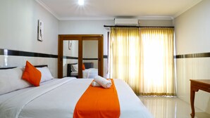 A hotel room with a neatly made bed, a wooden nightstand, a door, and a window with curtains. - Rena Segara House Kuta (Kuta)