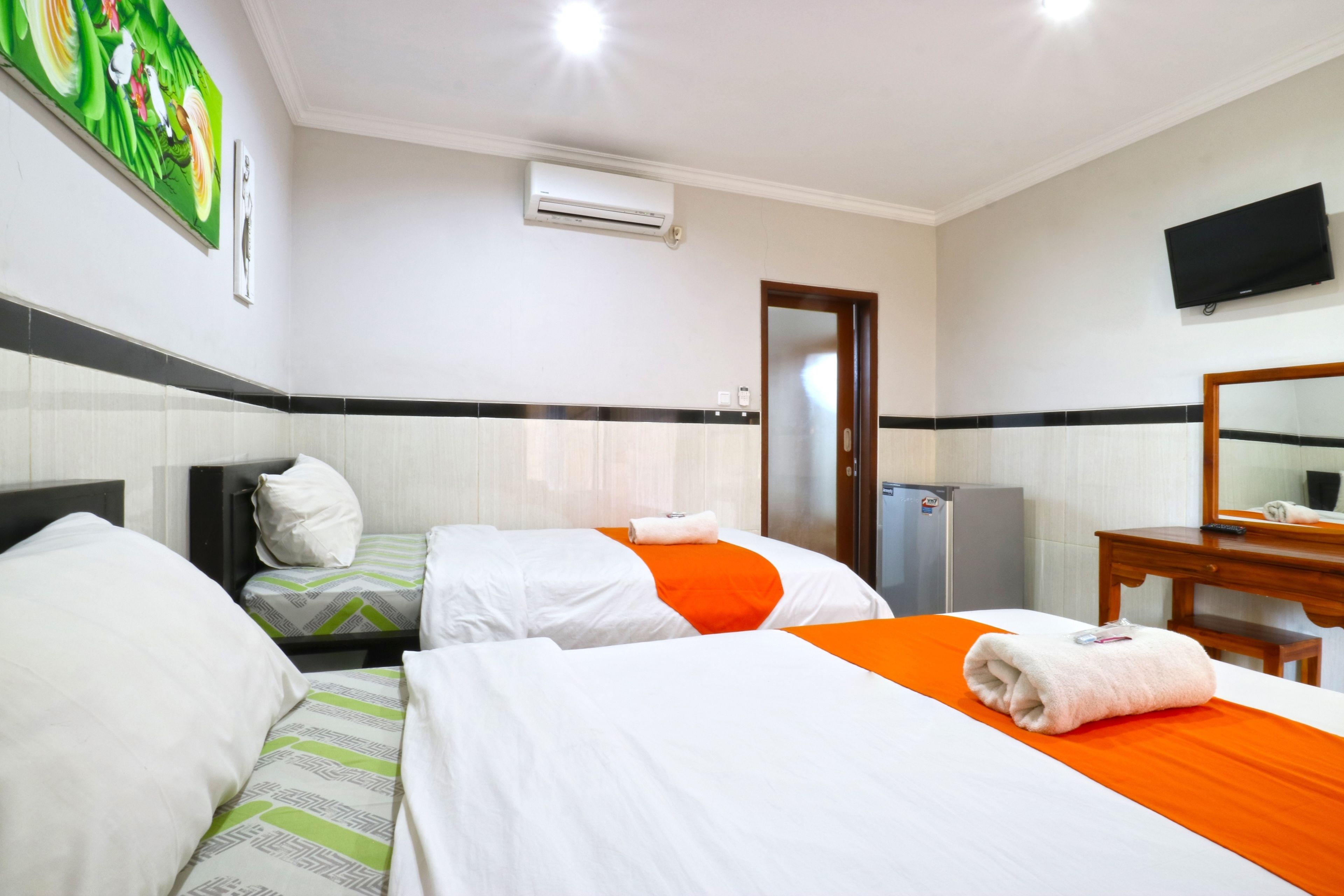 A hotel room with two beds, a television, a refrigerator, and a painting on the wall.