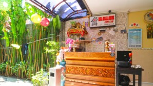 A reception area with a bamboo backdrop, a reception desk, and a wall-mounted sign indicating a 12:00 check-out time. - Rena Segara House Kuta (Kuta)