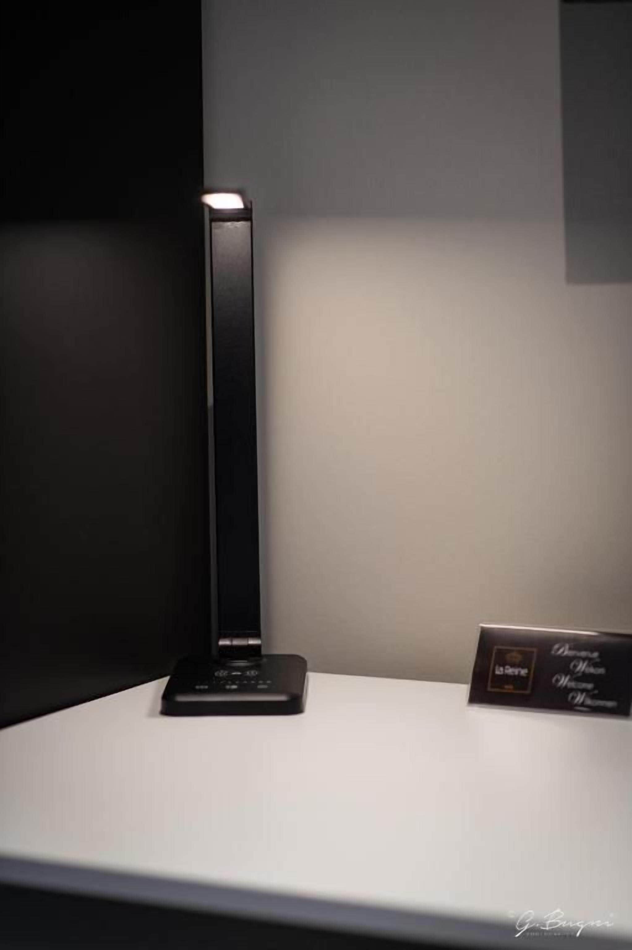 Eine schwarze Tischlampe auf einer weißen Oberfläche, mit einem Schild, auf dem 'La Scienza' steht.
