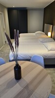 Una habitación de hotel con dos camas, una mesa redonda de madera y un florero con plumas de pampa, además de una mesita de noche con una lámpara.