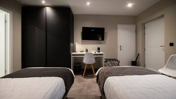 A bedroom with two beds, a desk, a chair, a TV, and a wardrobe.