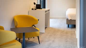 A modern hotel room with a yellow armchair, a small table, a white bedside table, and a bed.