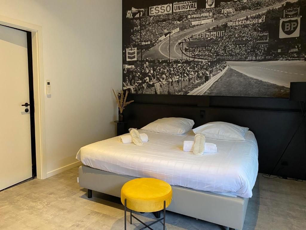A hotel room with a bed, a yellow stool, and a wall mural of a racing track.