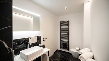 A modern bathroom with a white sink, black marble countertop, and a black towel rack with towels.