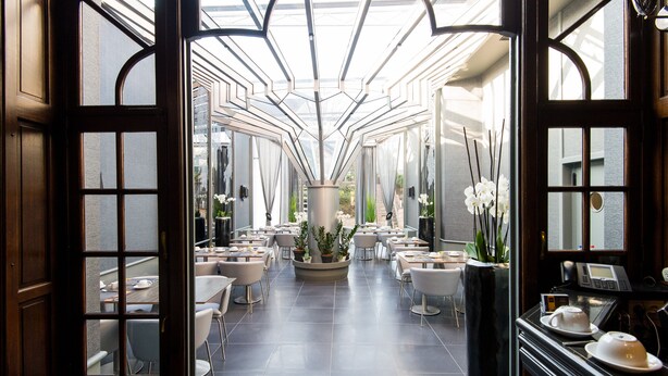 Un restaurante amplio y luminoso, con un macetero central, mobiliario moderno y techo de cristal.