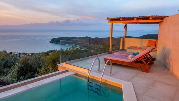 A private pool with a glass barrier, a lounge chair, and a pergola overlooking a coastal view.