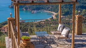 A wooden pergola with a tiled roof overlooking a coastal bay with boats.