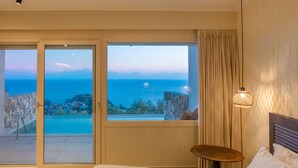 A hotel room with a bed, a small table, and a view of the sea through large windows.