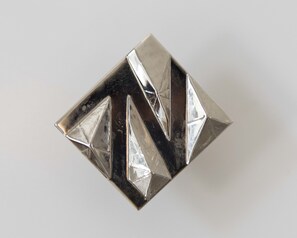 A geometric, metallic object with a reflective surface, possibly a decorative item or jewelry.