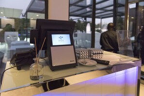 A reception desk with a digital display, a cash register, a glass bottle, and a remote control.